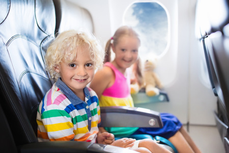 85244121 - child in airplane. kids sit in air plane window seat. flight entertainment for kid. traveling with young children. kids fly and travel. family summer vacation. girl and boy with toy in airplane.